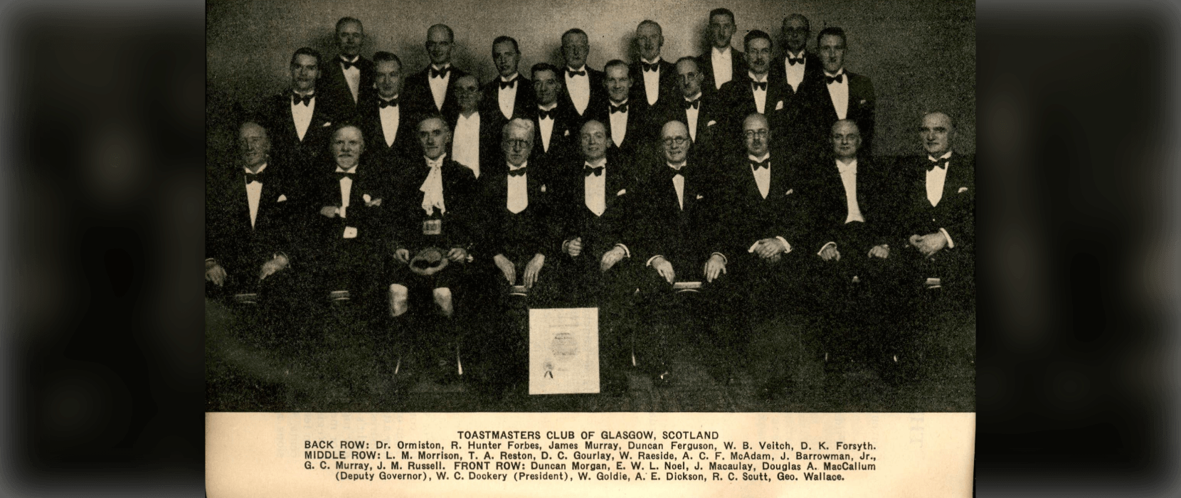 Large group of men wearing tuxedos sitting in rows
