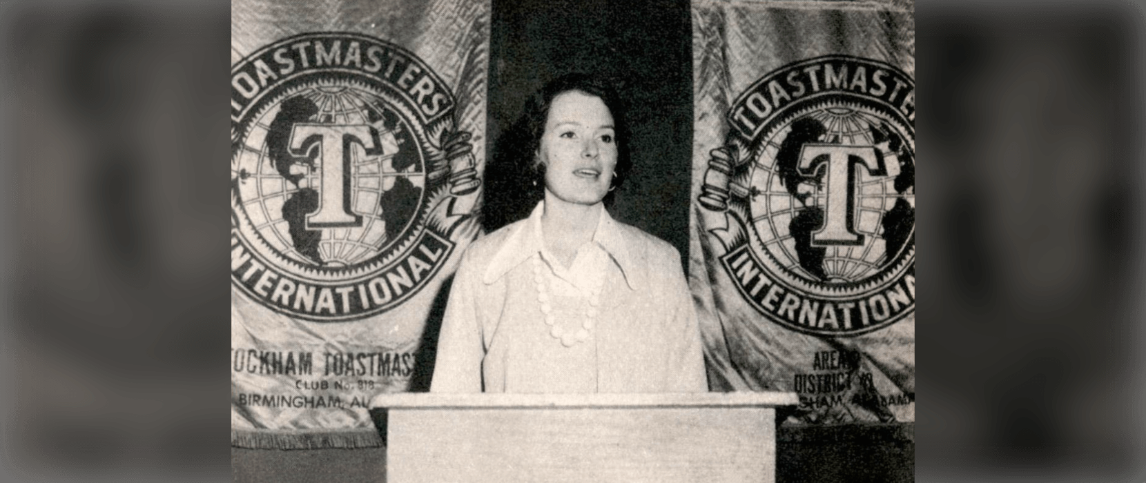 Black and white image of a woman speaking at a lectern