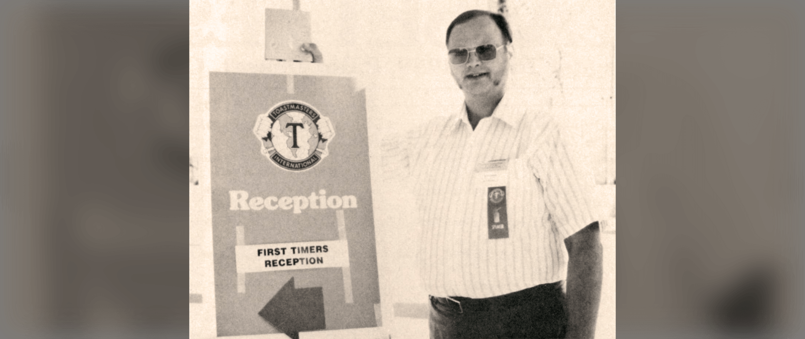 Black and white photo of a man standing next to a sign