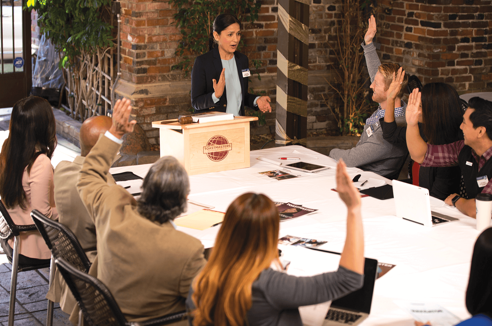 Female standing at Toastmasters lectern while members raise their hands
