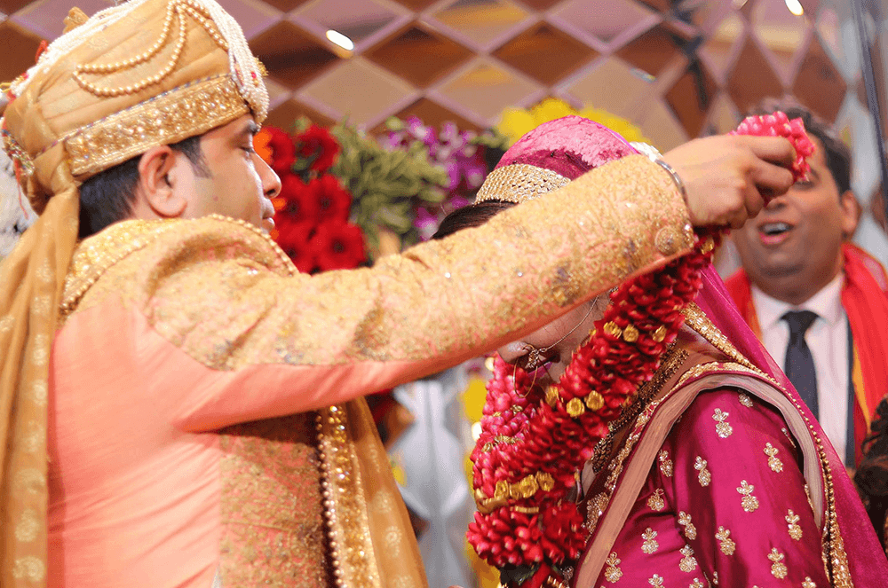 Man placing garland over bride’s head