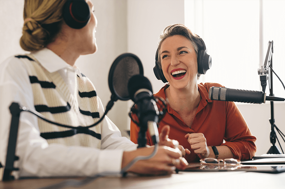 Two women wearing headphones speaking into microphones during podcast interview