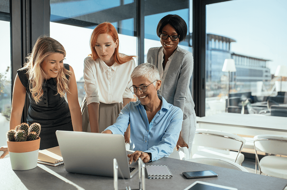 Four female coworkers gathered around laptop smiling
