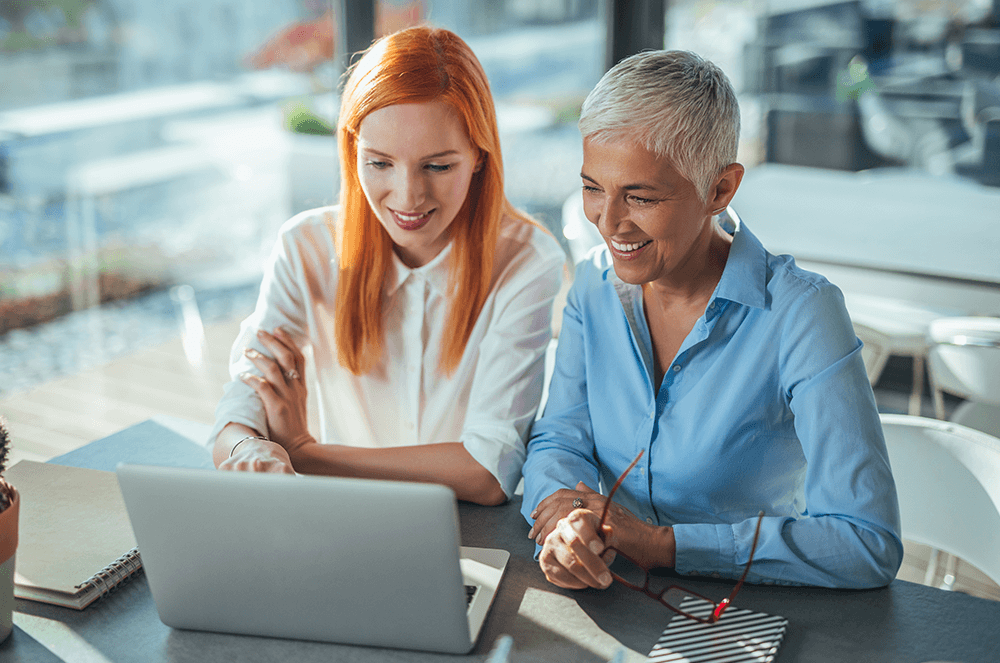 Two women sitting at laptop working and smiling