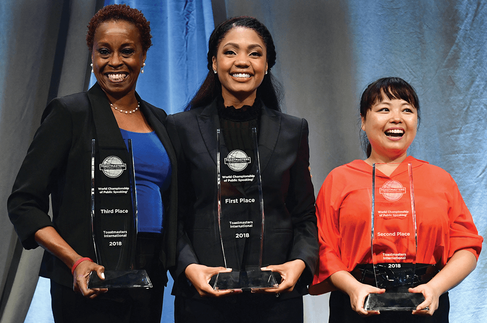 Three women holding trophies after winning speech contest
