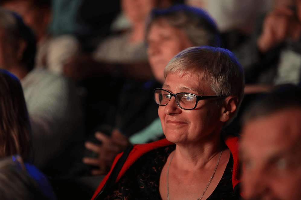 Woman in glasses smiling while she listens to someone speak