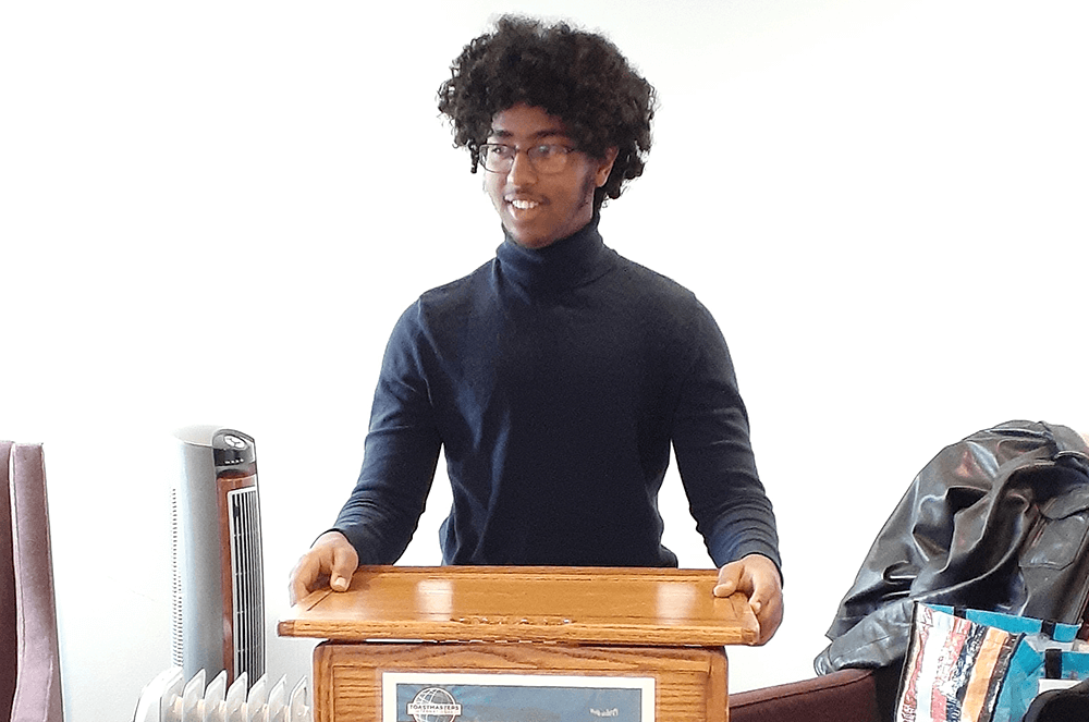 Eighteen-year-old man in blue turtleneck standing at lectern