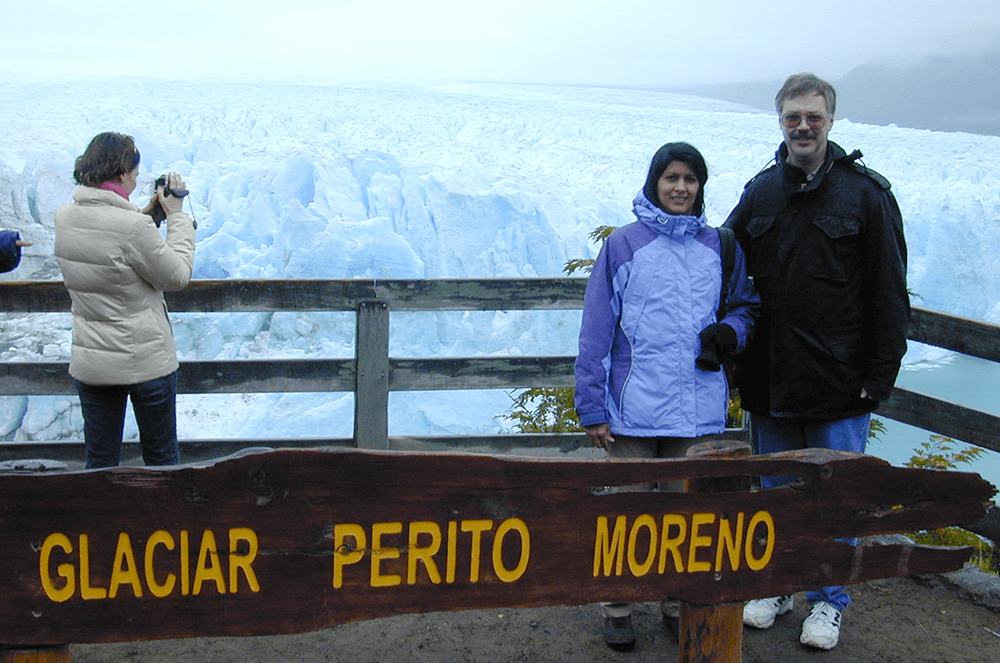 Man and woman posing near sign with Perito Moreno Glacier in background