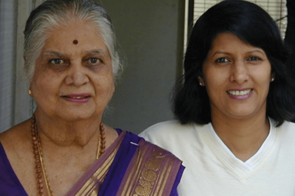 Mother in purple dress and gold saree posing with daughter in white shirt