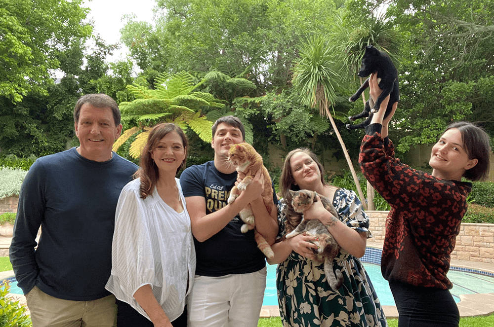 Family with husband, wife, three children, and three pets posing outdoors near pool